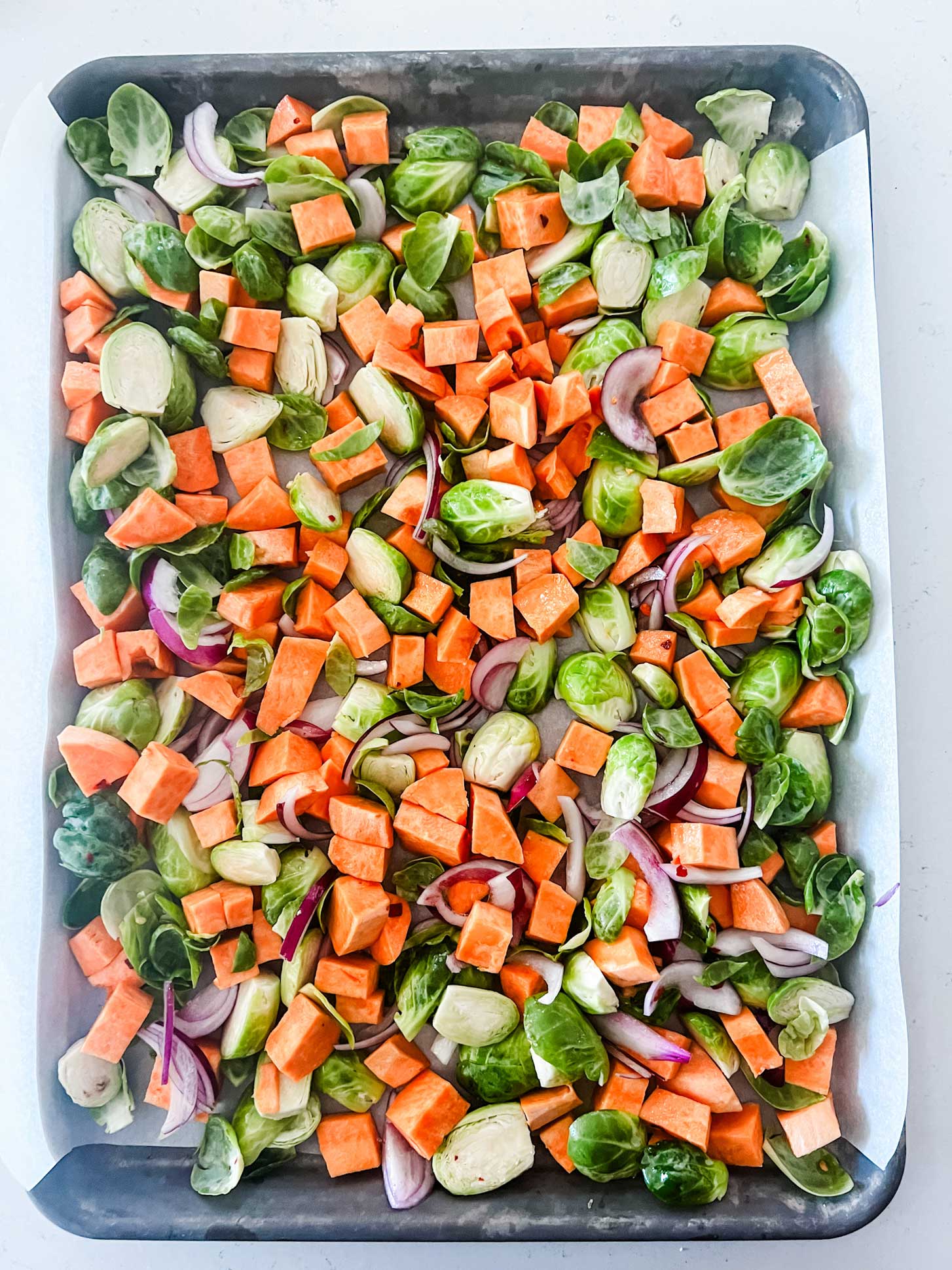 A sheet pan with brussels sprouts, sweet potatoes, and red onion ready for the oven.