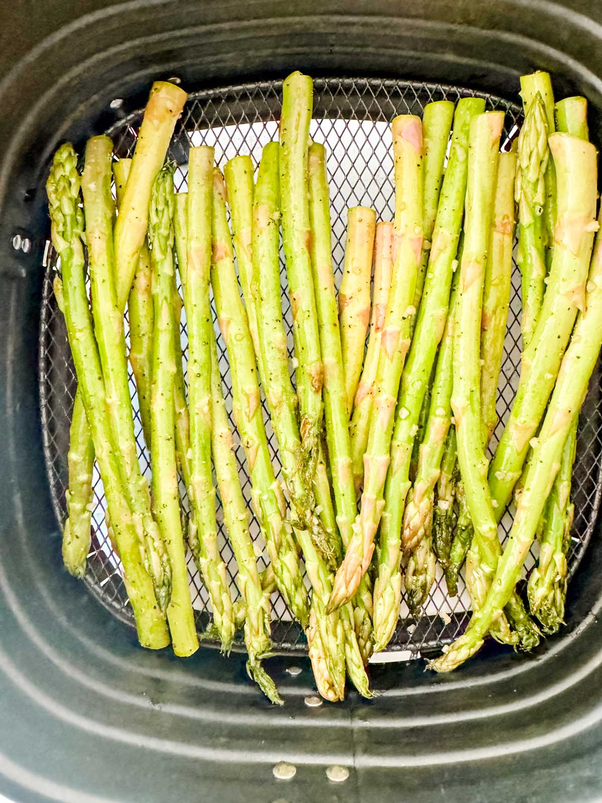Uncooked asparagus in an air fryer basket.