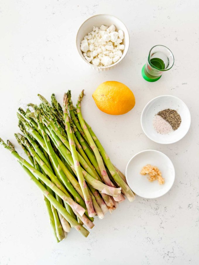 Overhead photo of asparagus, goat cheese, lemon, oil, seasonings, and garlic.