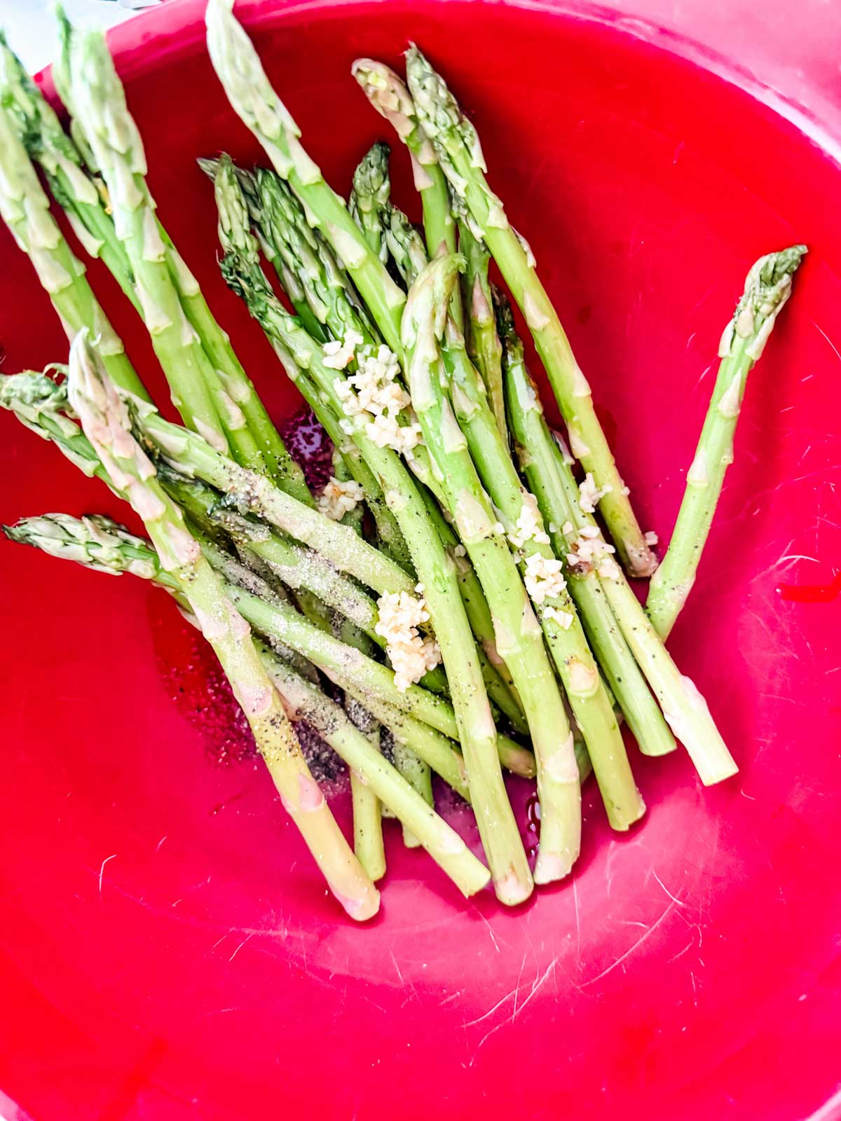 Asparagus in a bowl with garlic, oil, and seasonings.