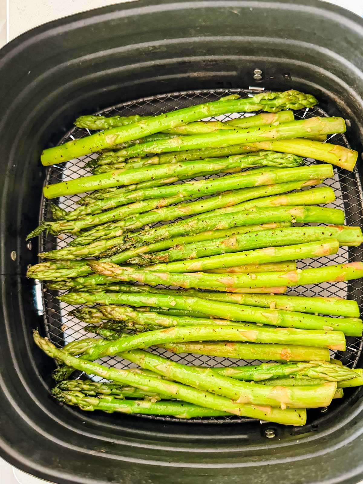 Cooked asparagus in an air fryer basket.