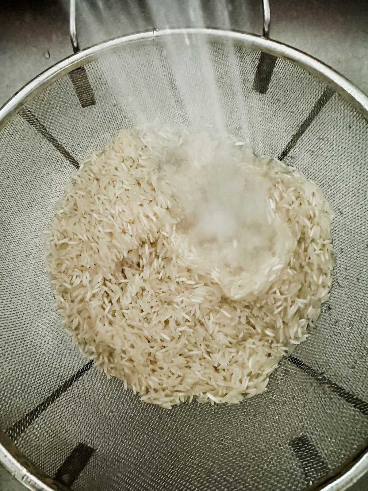Rice in a strainer being rinsed.
