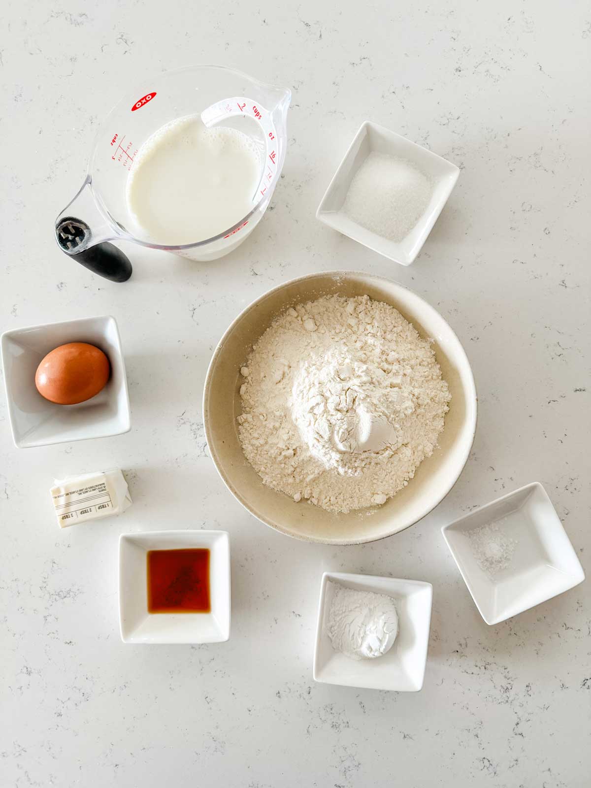 Overhead photo of flour, milk, egg, butter, vanilla, sugar, salt, and baking powder.