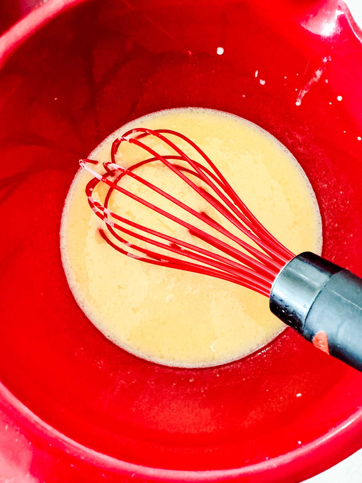 Wet ingredients for pancakes in a red bowl with a whisk.