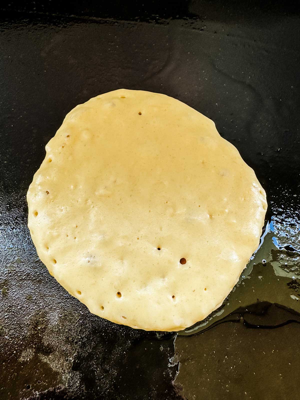 A pancake on a griddle that is ready to flip.