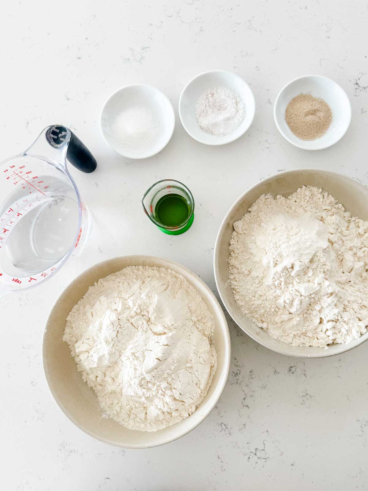 Overhead photo of bread flour, all purpose flour, yeast, salt, sugar, oil, and water.