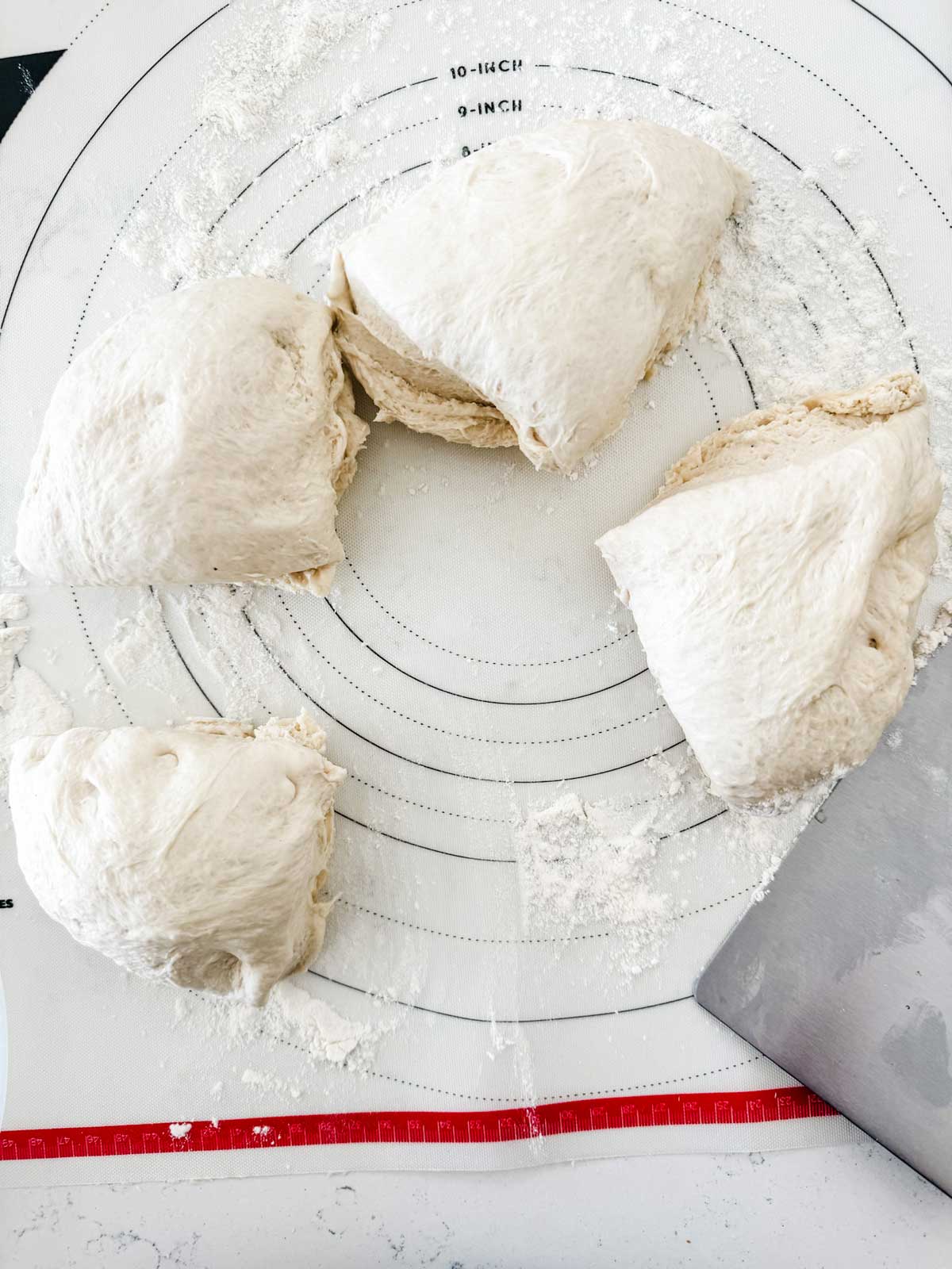 Photo of pizza dough divided into quarters with a pastry knife.