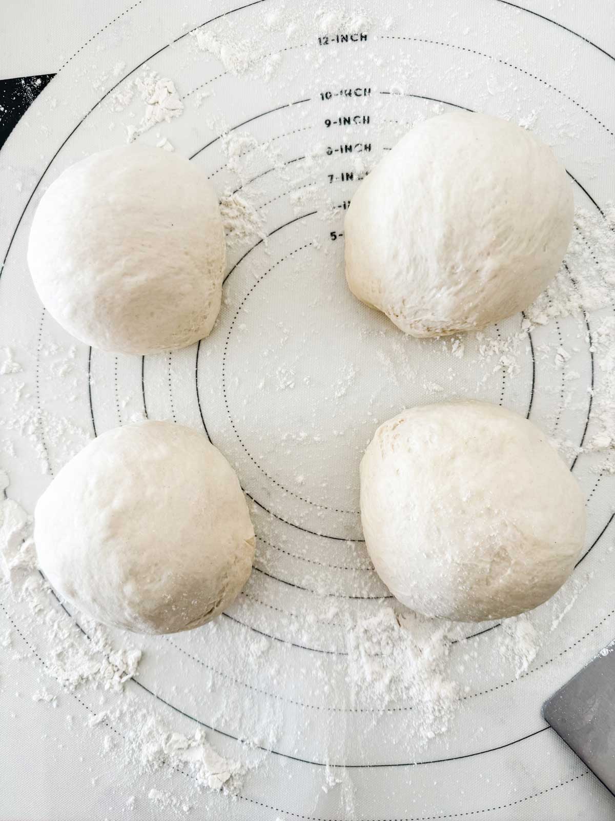 Photo of pizza dough separated into four rounds.