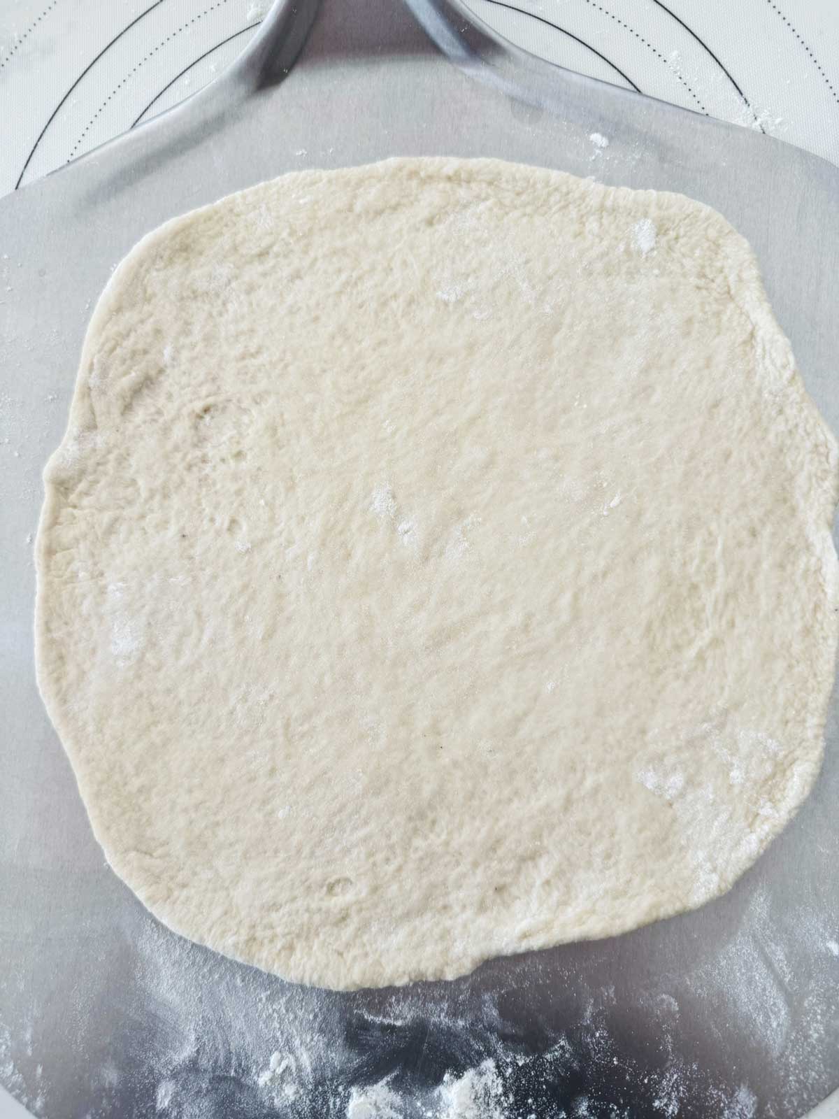 A rolled out pizza crust on a lightly floured pizza peel.