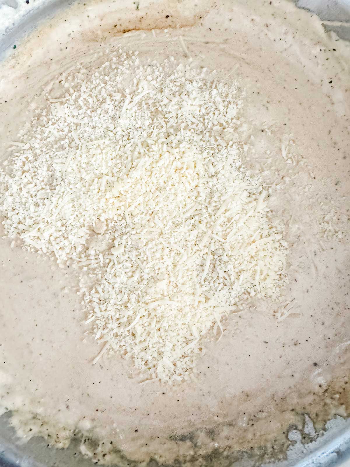 Parmesan cheese being added to a cream sauce.