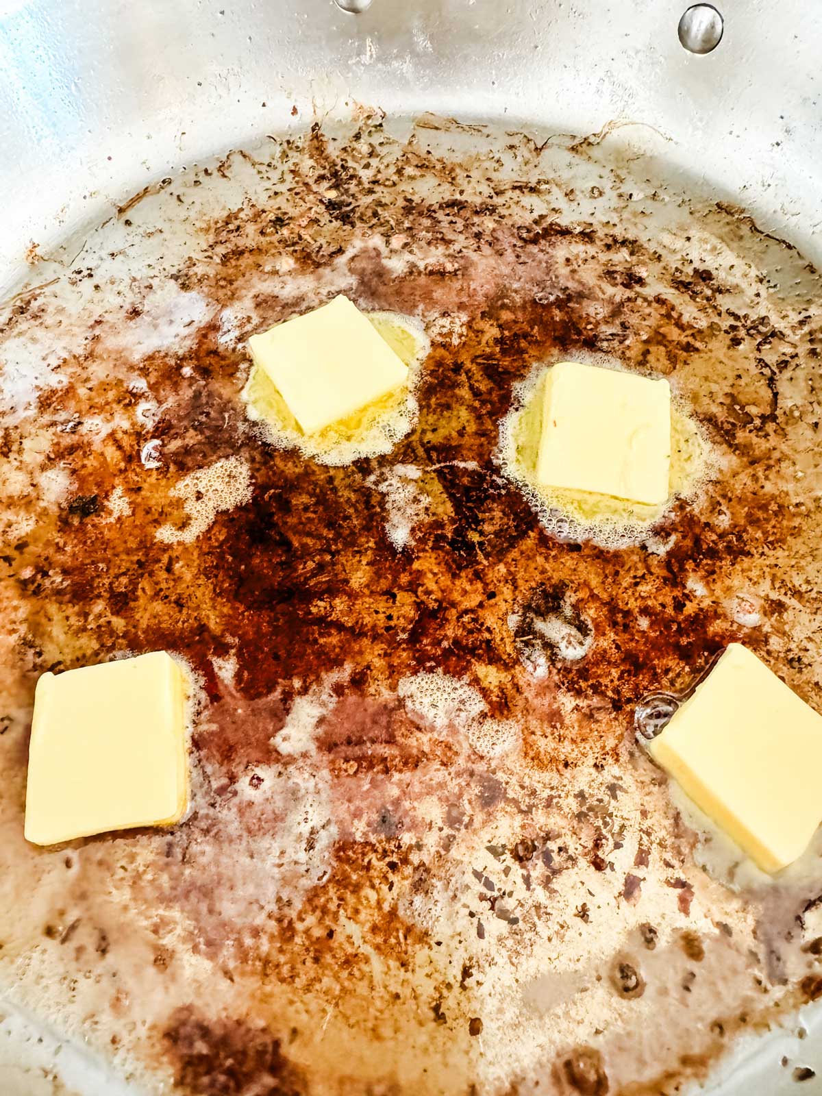 Butter being added to a skillet of bacon grease.