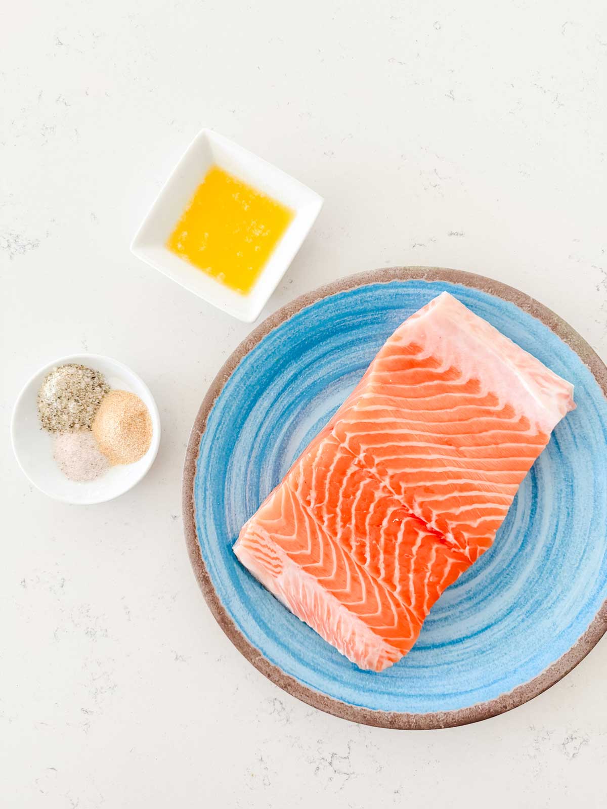 Overhead photo of a salmon fillet, oil, and seasonings.