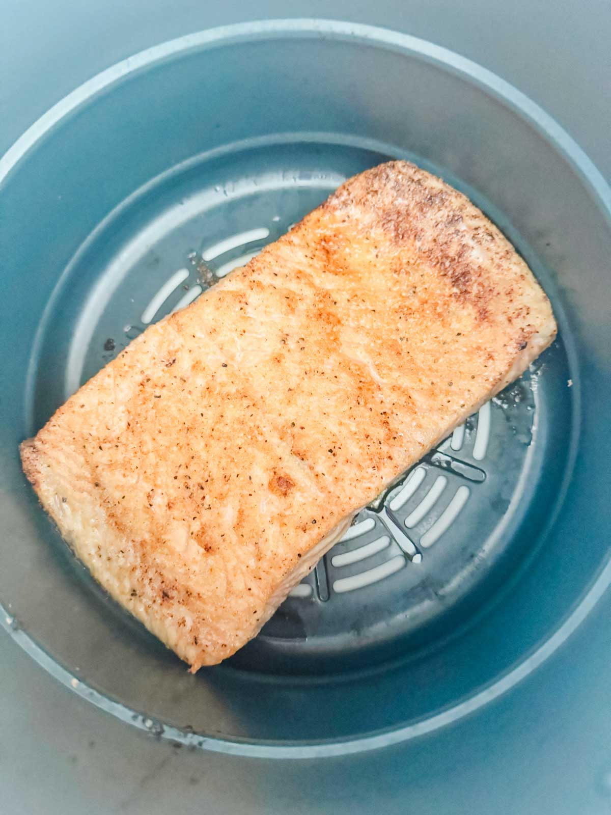 Salmon that has been almost all the way cooked in a Ninja Foodi air fryer basket.