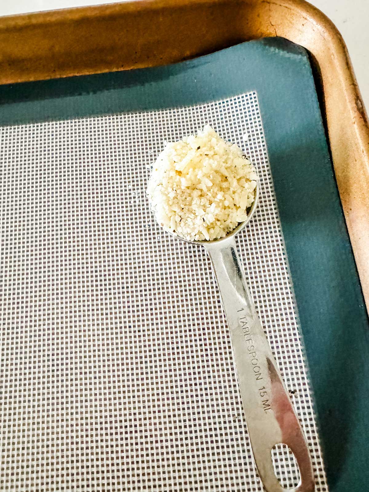 A tablespoon measure with finely grated parmesan, arrowroot and pepper.