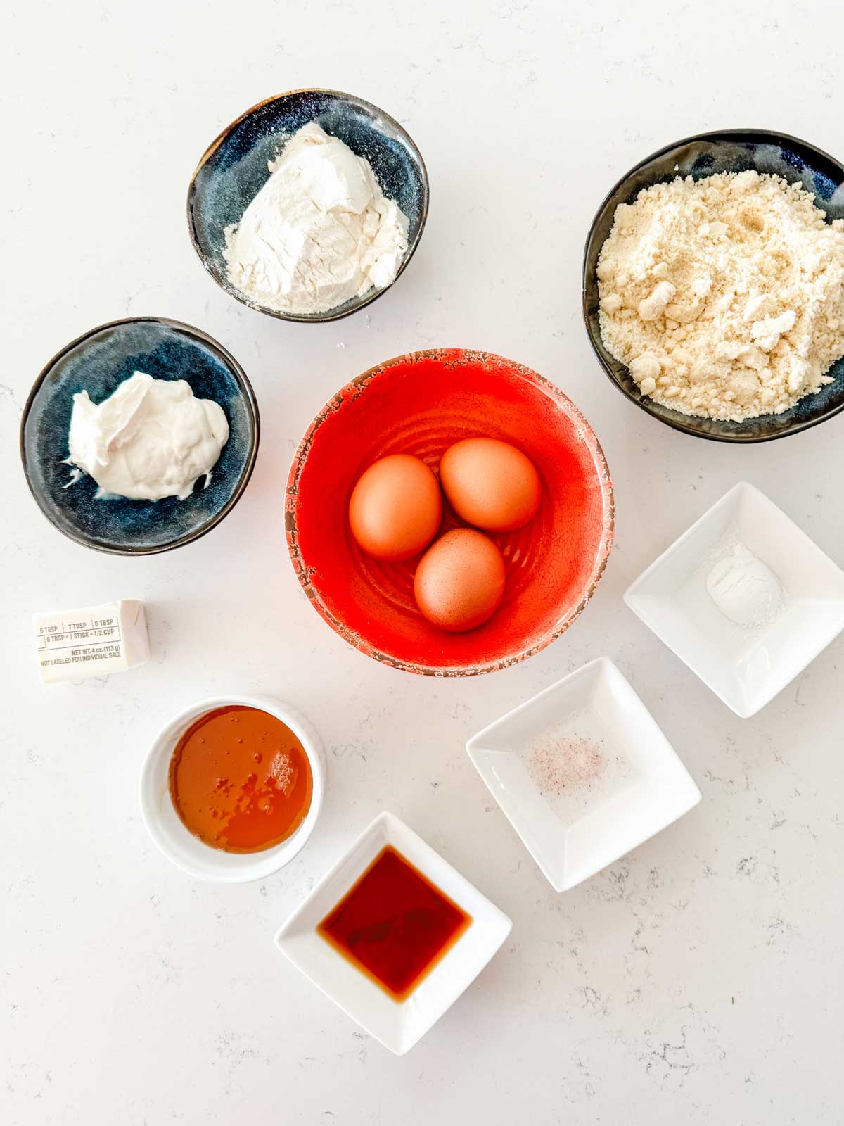 Overhead photo of three eggs, almond flour, flour, yogurt, honey, vanilla, salt, and baking powder.