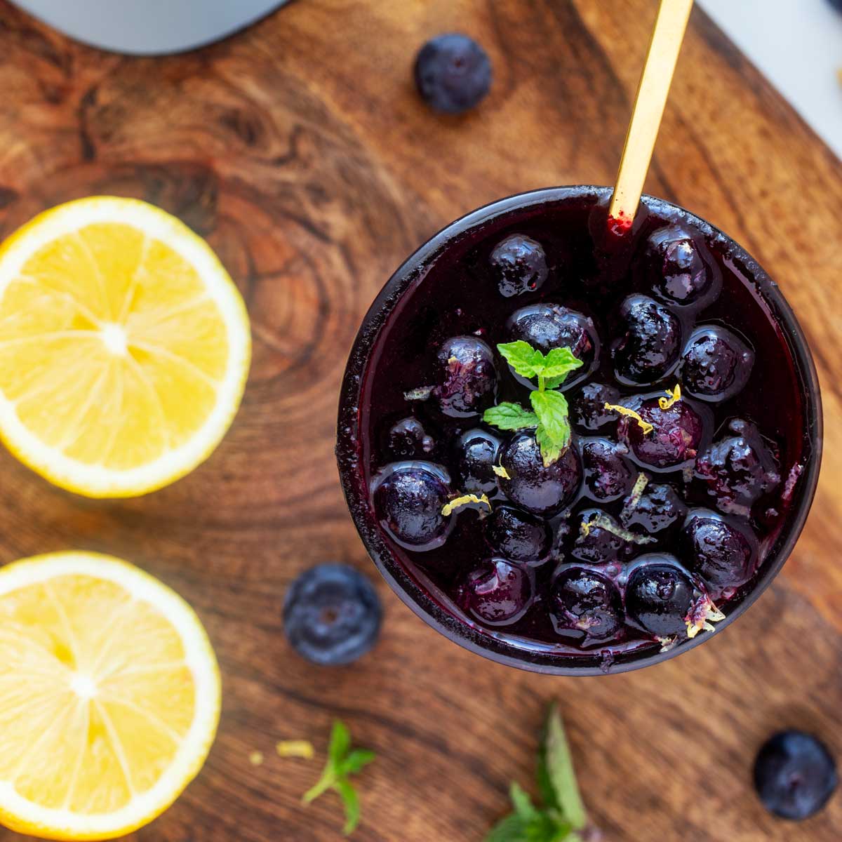 Overhead square photo of blueberry compote in a glass jar garnished with mint.