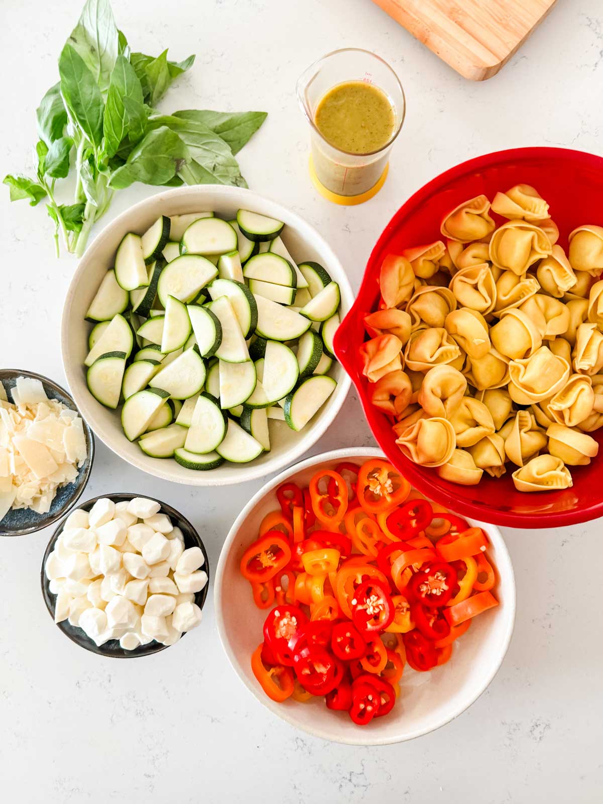 Overhead photo of a bowl of tortellini, zucchini, baby peppers, fresh mozzarella, parmesan, basil, and Italian dressing.