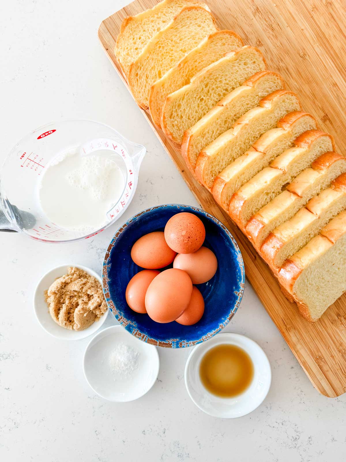 Overhead photo of brioche bread, eggs, vanilla, sugar, cream, and salt.