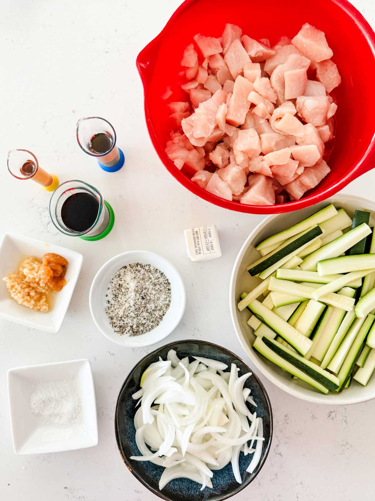 Overhead photo of chicken, salt, pepper, soy sauce, butter, minced garlic, sesame oil, ginger, zucchini, and onion.

