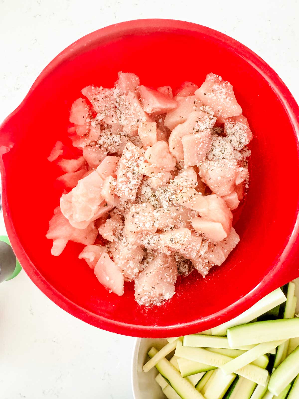 Cubed chicken with seasonings in a red bowl.