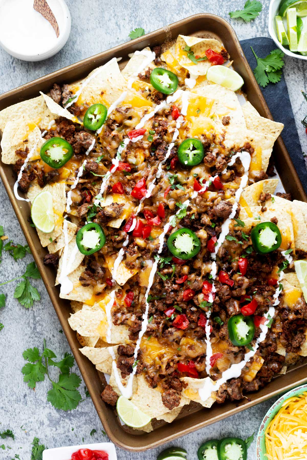 Overhead photo of a sheet pan with Blackstone nachos garnished with sour cream and jalapenos.