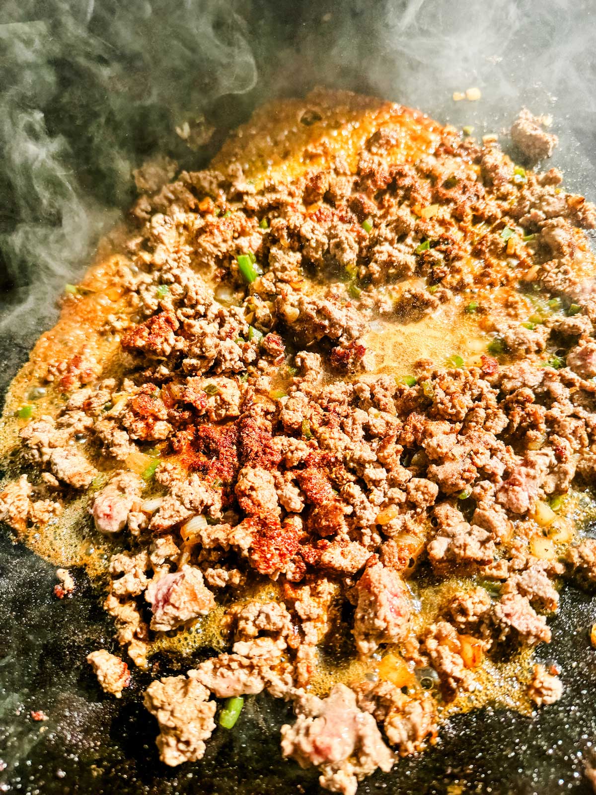 Water being added to ground beef to make saucy taco seasoned meat.