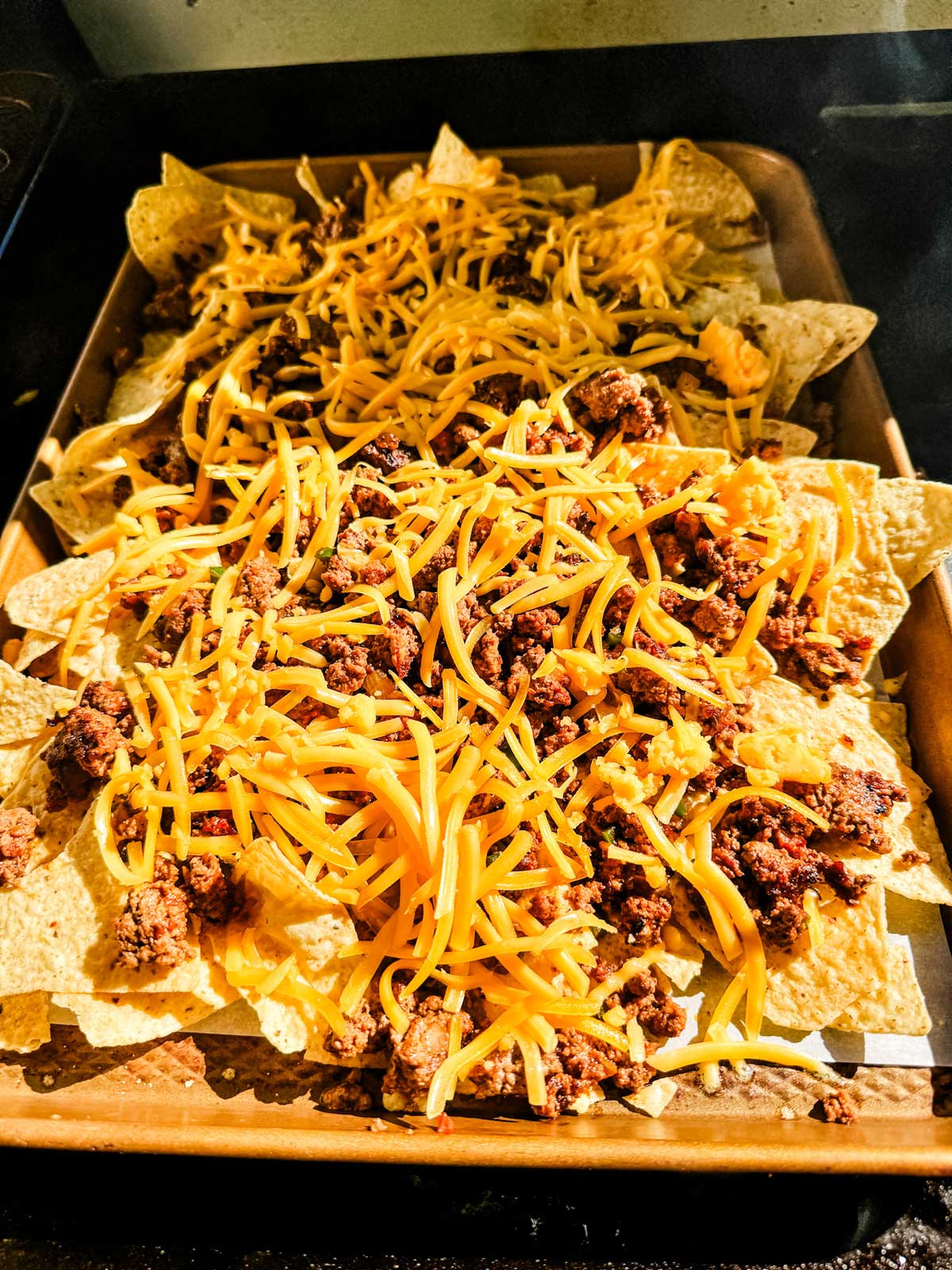 Nachos that have just had cheese sprinkled on top of them.