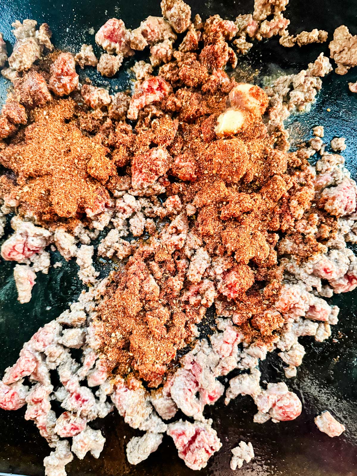 Taco seasoning over partially cooked ground beef on a Blackstone griddle.