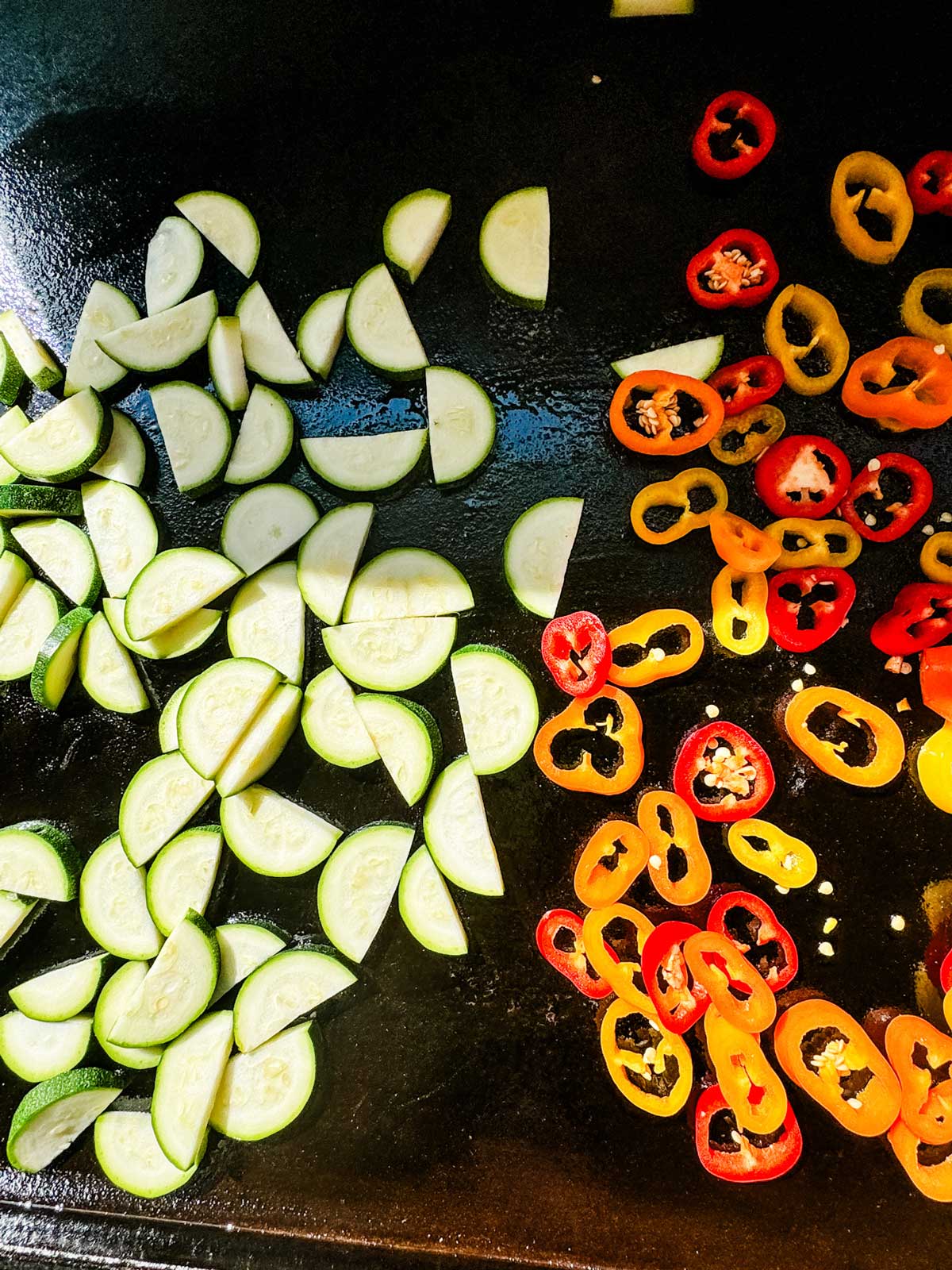 Zucchini and sliced baby peppers added to a blackstone griddle.