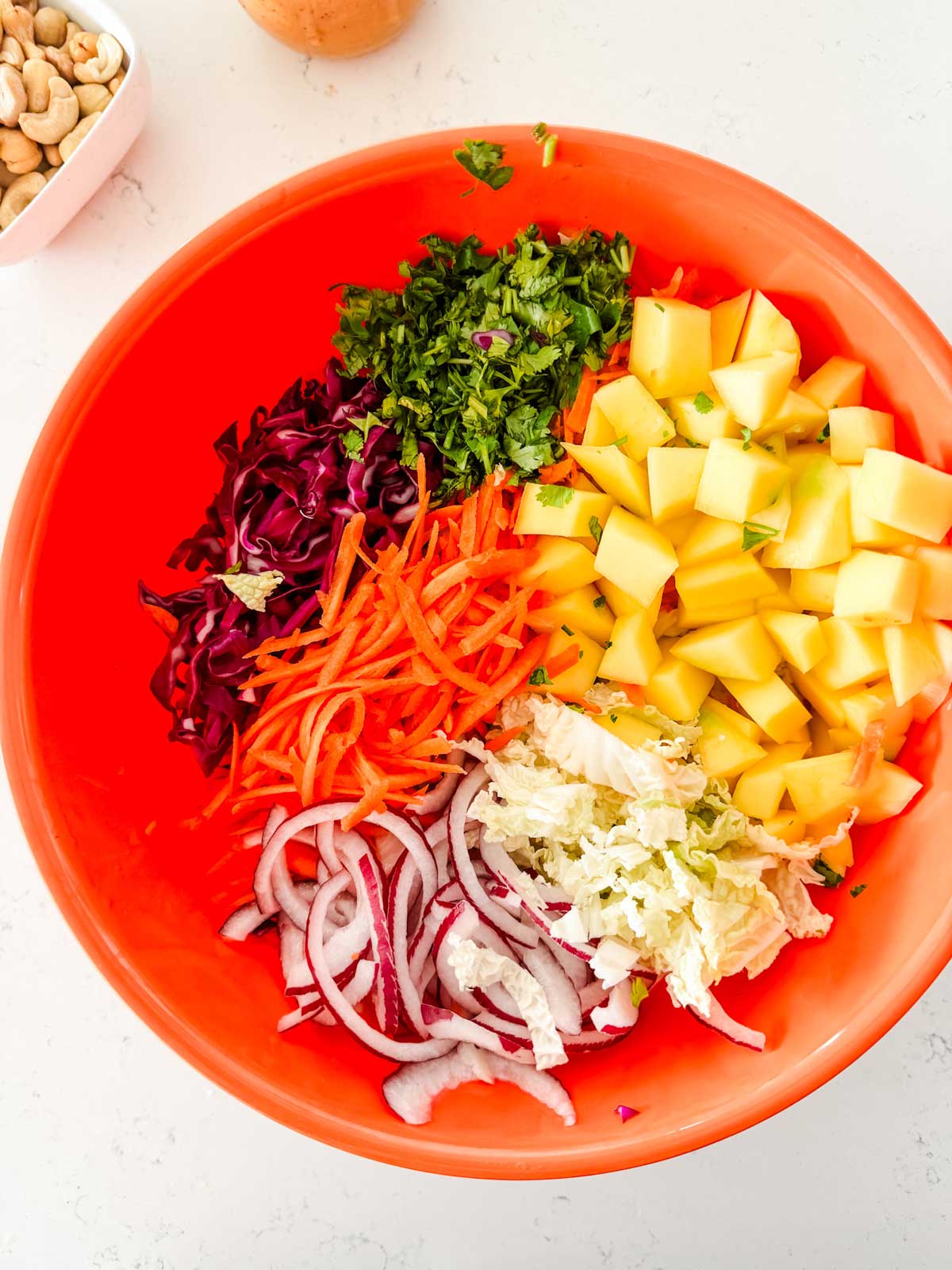 An orange bowl with napa cabbage, diced mango, red onion, carrots, cabbage, and cilantro.