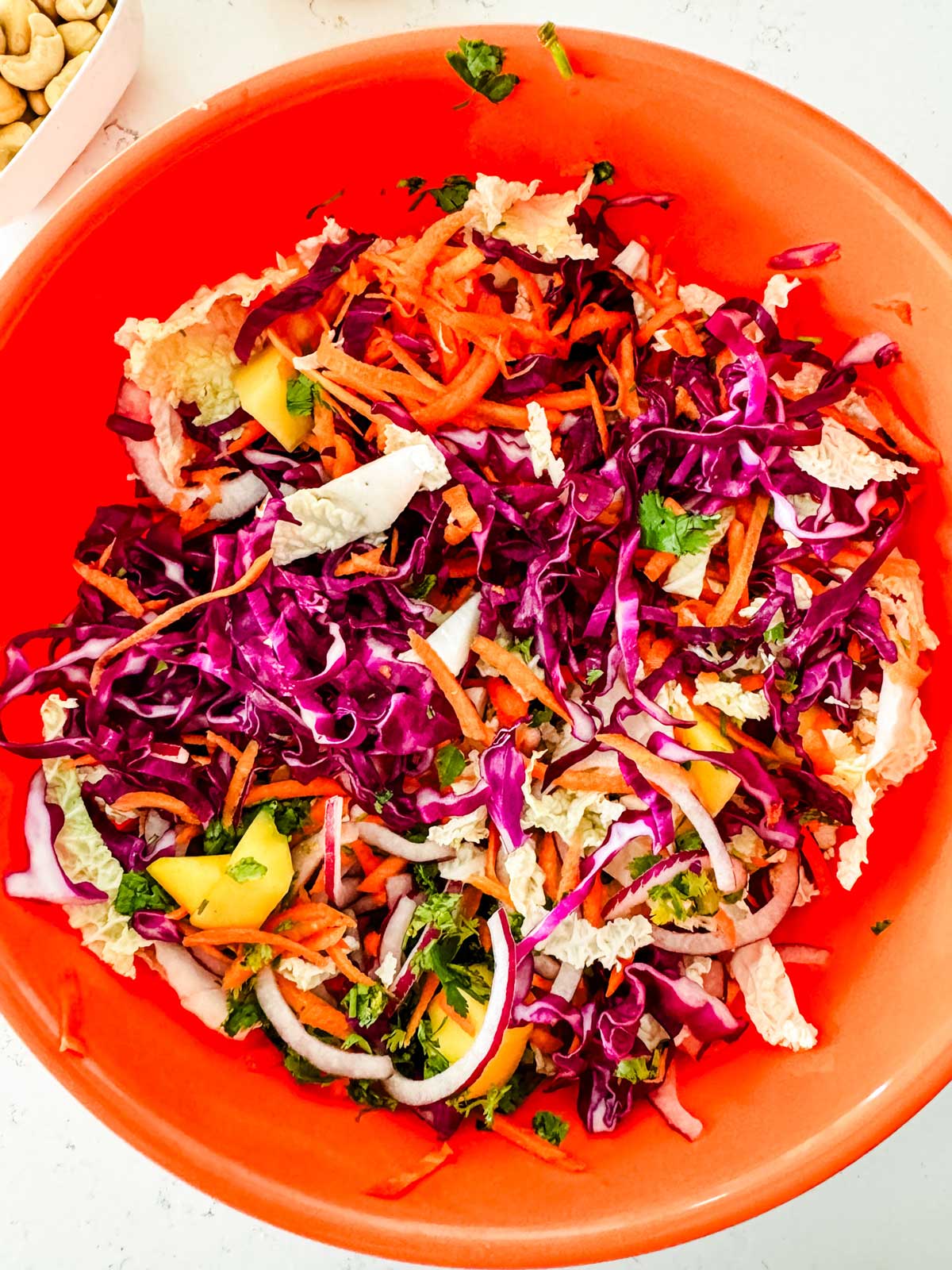 Napa cabbage, diced mango, red onion, carrots, cabbage, and cilantro tossed together in a lareg orange bowl.