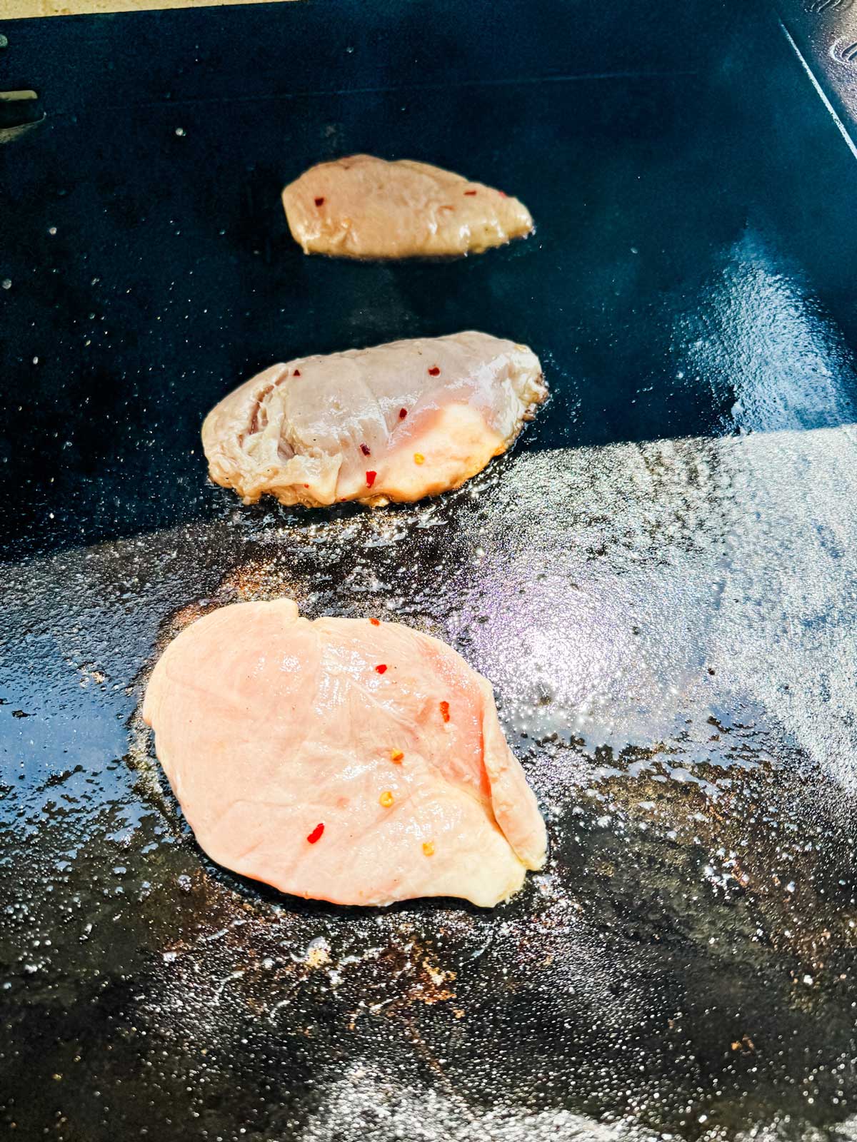 Raw marinated chicken just added to a Blackstone griddle.