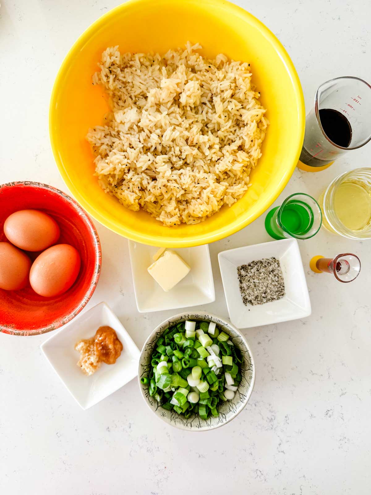 Overhead photo of cooked rice, eggs, butter, green onion, garlic, ginger, soy sauce, oil, sesame oil, and rice wine vinegar.