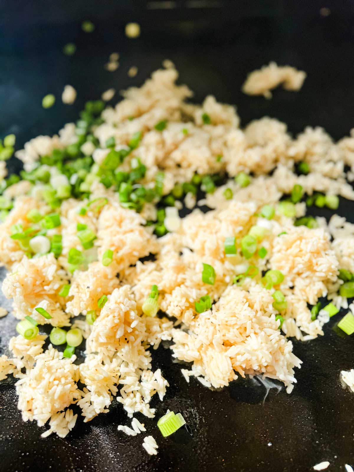 Rice and scallions cooking on a flat top griddle.