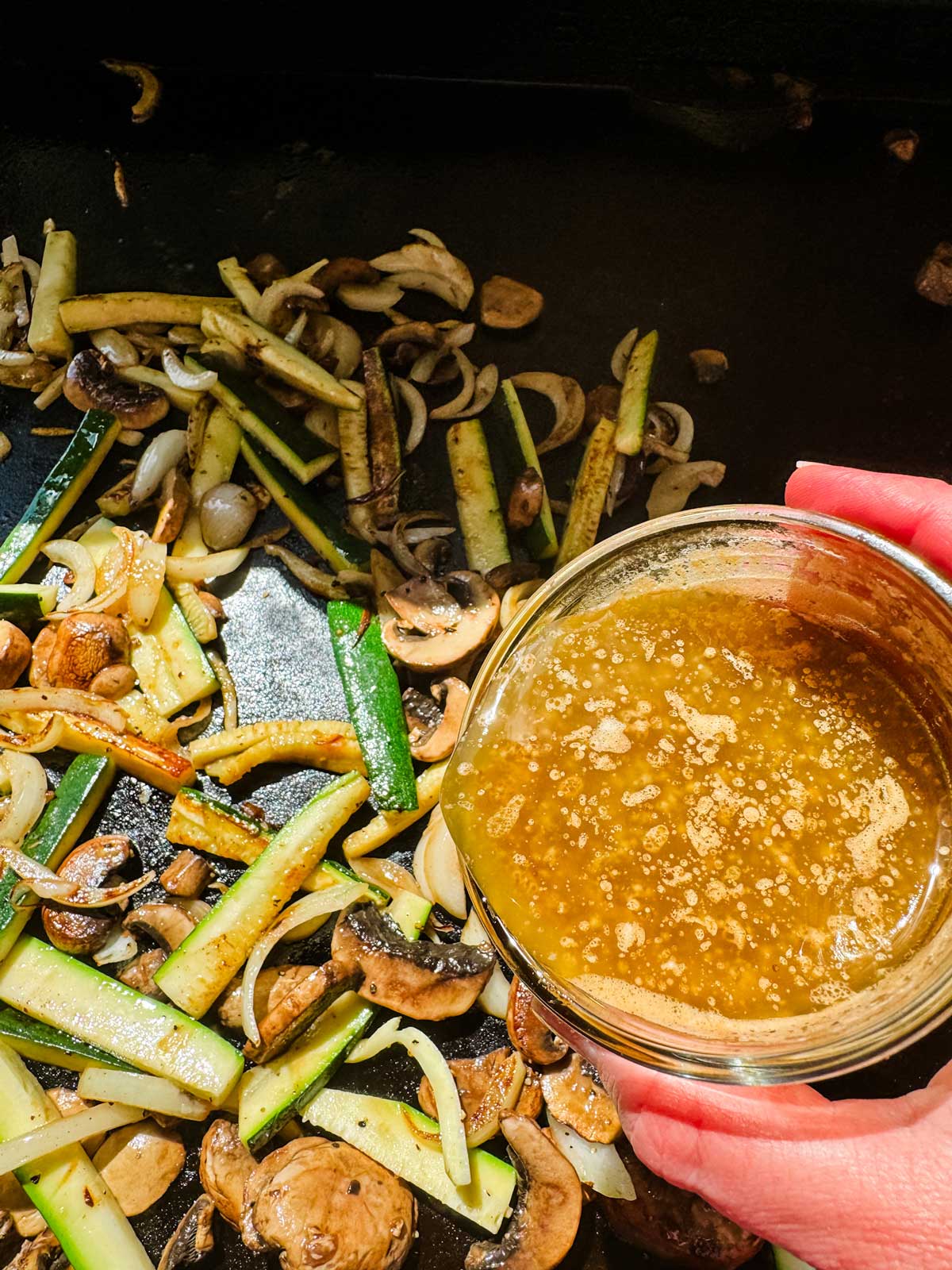 Soy garlic butter being poured on the vegetables on a flat top griddle.