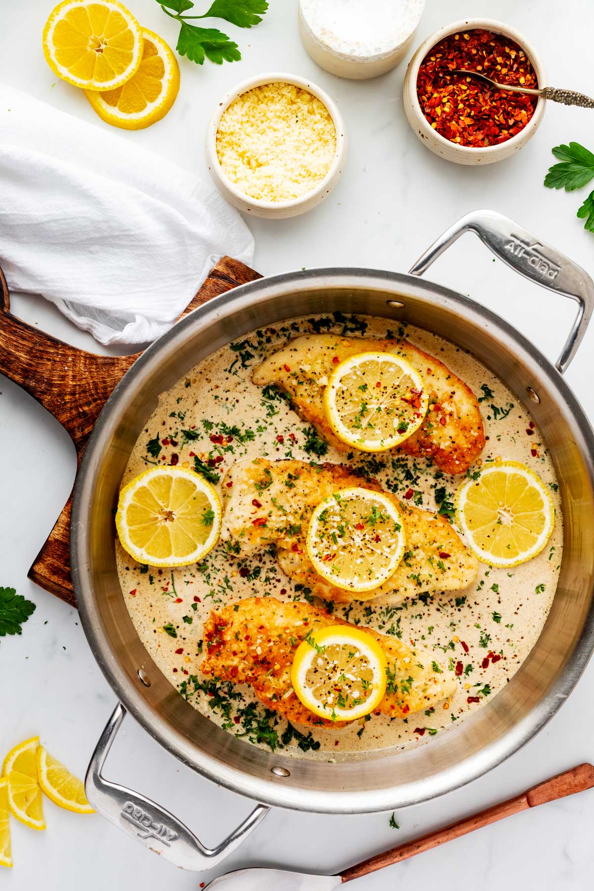 Photo of a skillet with lemon pepper chicken garnished with lemons, parsley, and red pepper flakes.