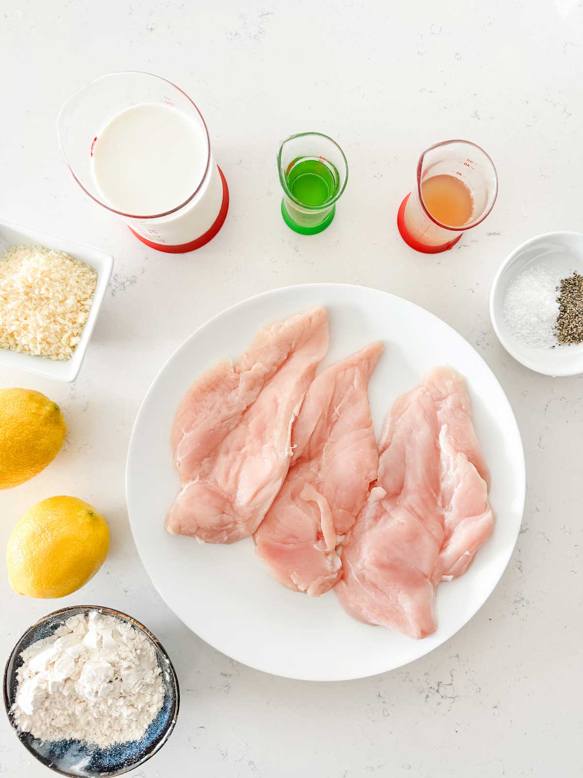 Overhead photo of chicken, flour, lemons, parmesan, cream, oil, broth, and seasonings.