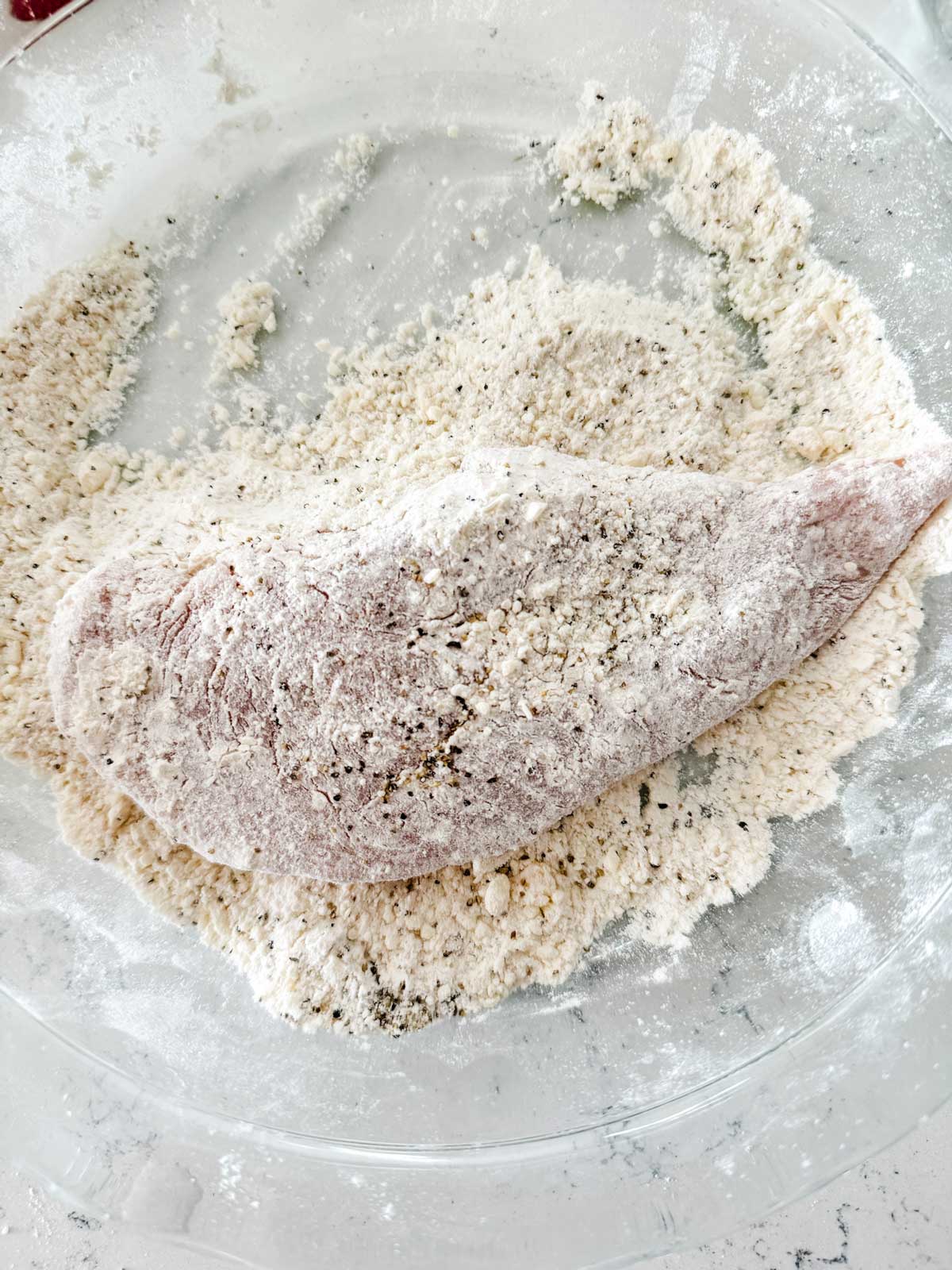Chicken being dredged in a flour coating.