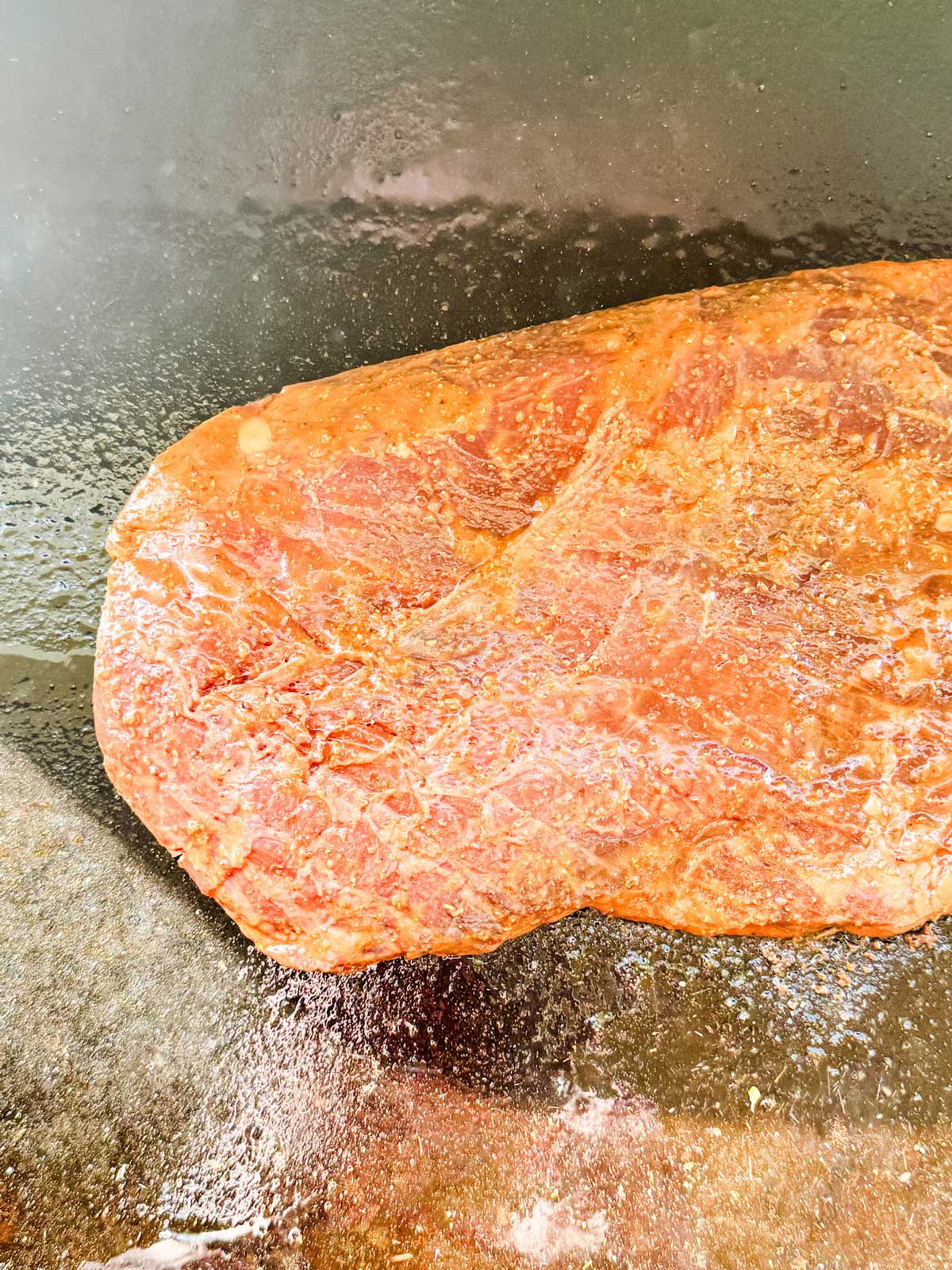 Flank steak cooking on a hot griddle.