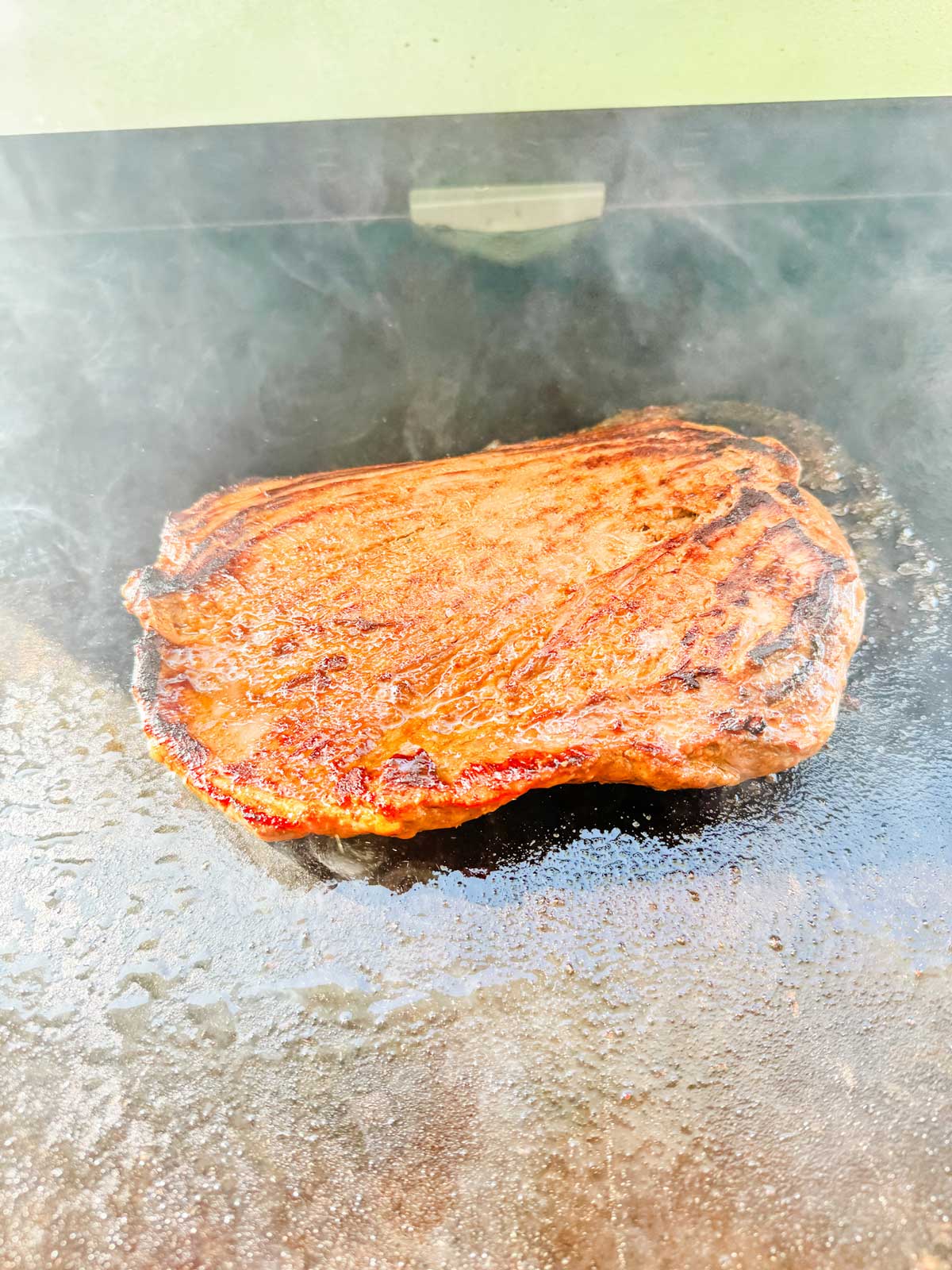 Flank steak cooking on a griddle.