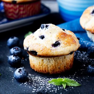 Square side photo of a buttermilk blueberry muffin sitting next to fresh blueberries and mint.