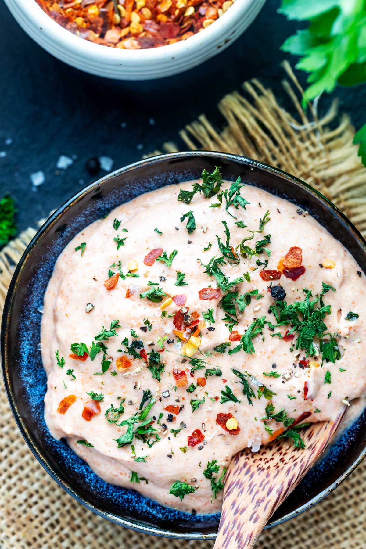Close up photo of a bowl of yum yum sauce garnished with parsley and crushed red pepper flakes.