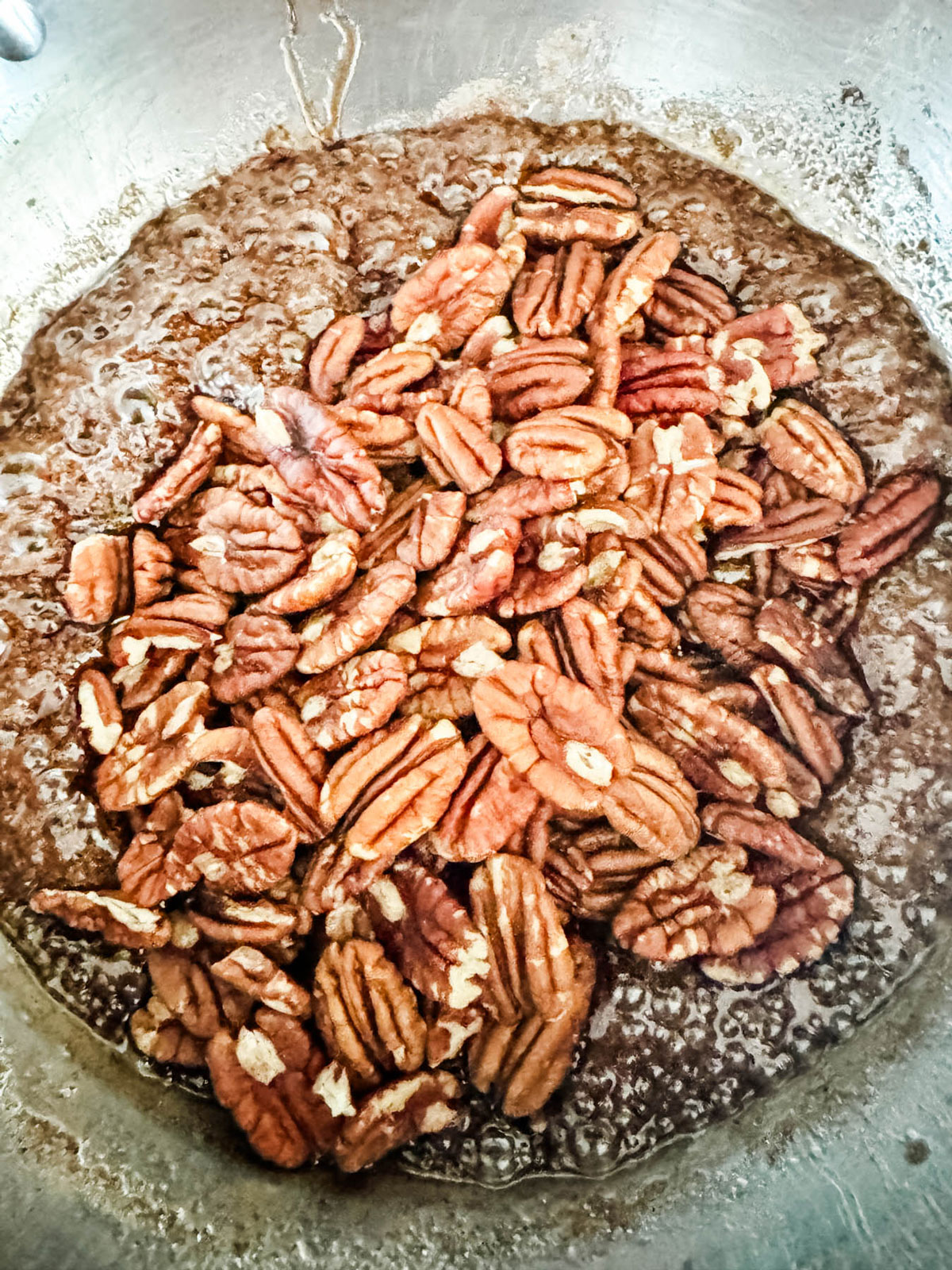 Pecans just added to a spiced sugar mixture in a saucepan.