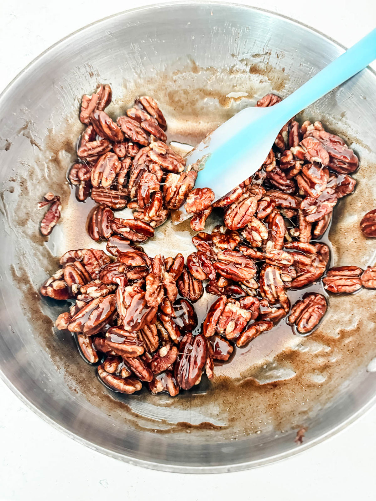 Pecans being stirred into a spiced sugar mixture in a saucepan.