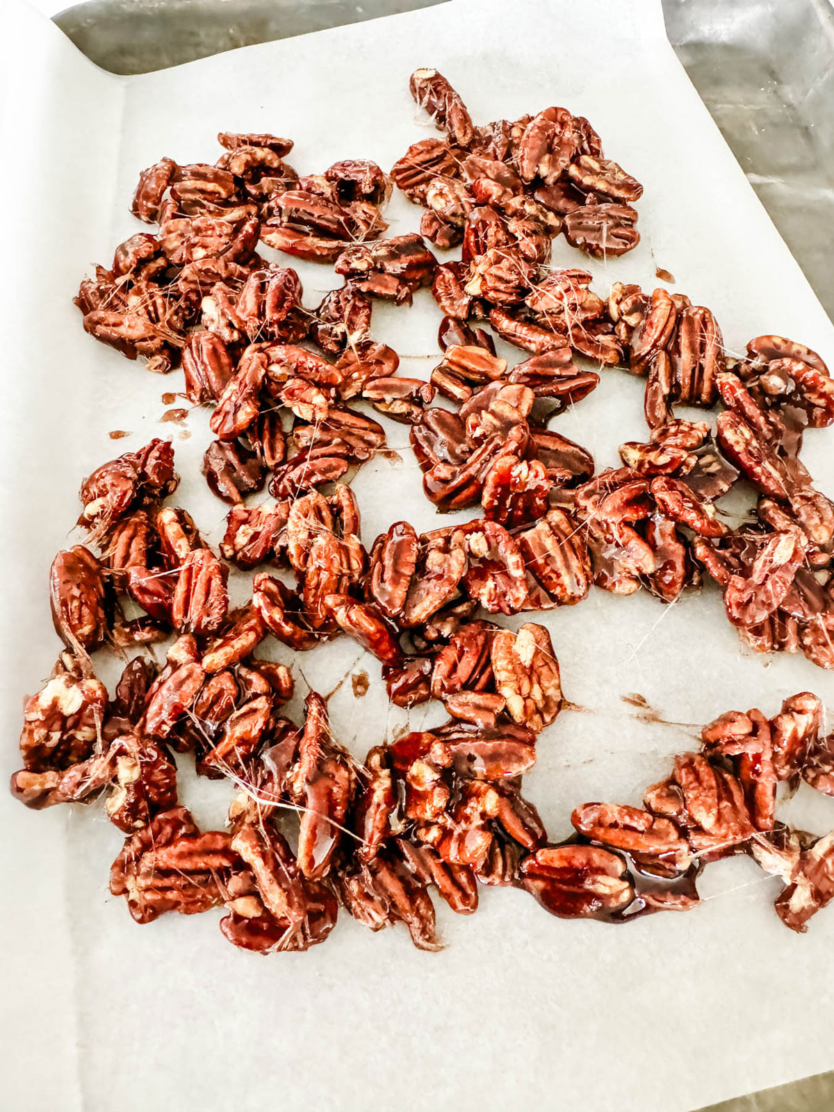 Candied spiced pecans cooling on a parchment lined baking sheet.