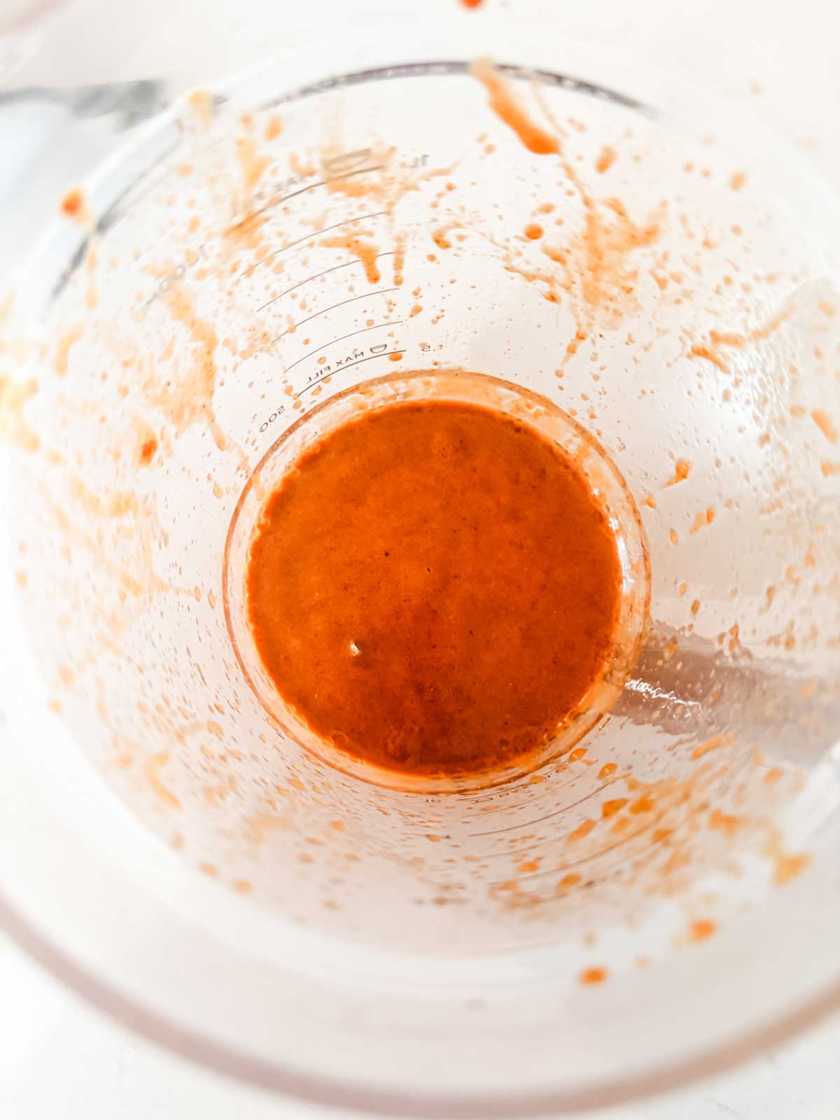 A close-up top view of a glass mixing bowl with remnants of a bright orange sauce or dressing coating the sides and a small amount pooled at the bottom.
