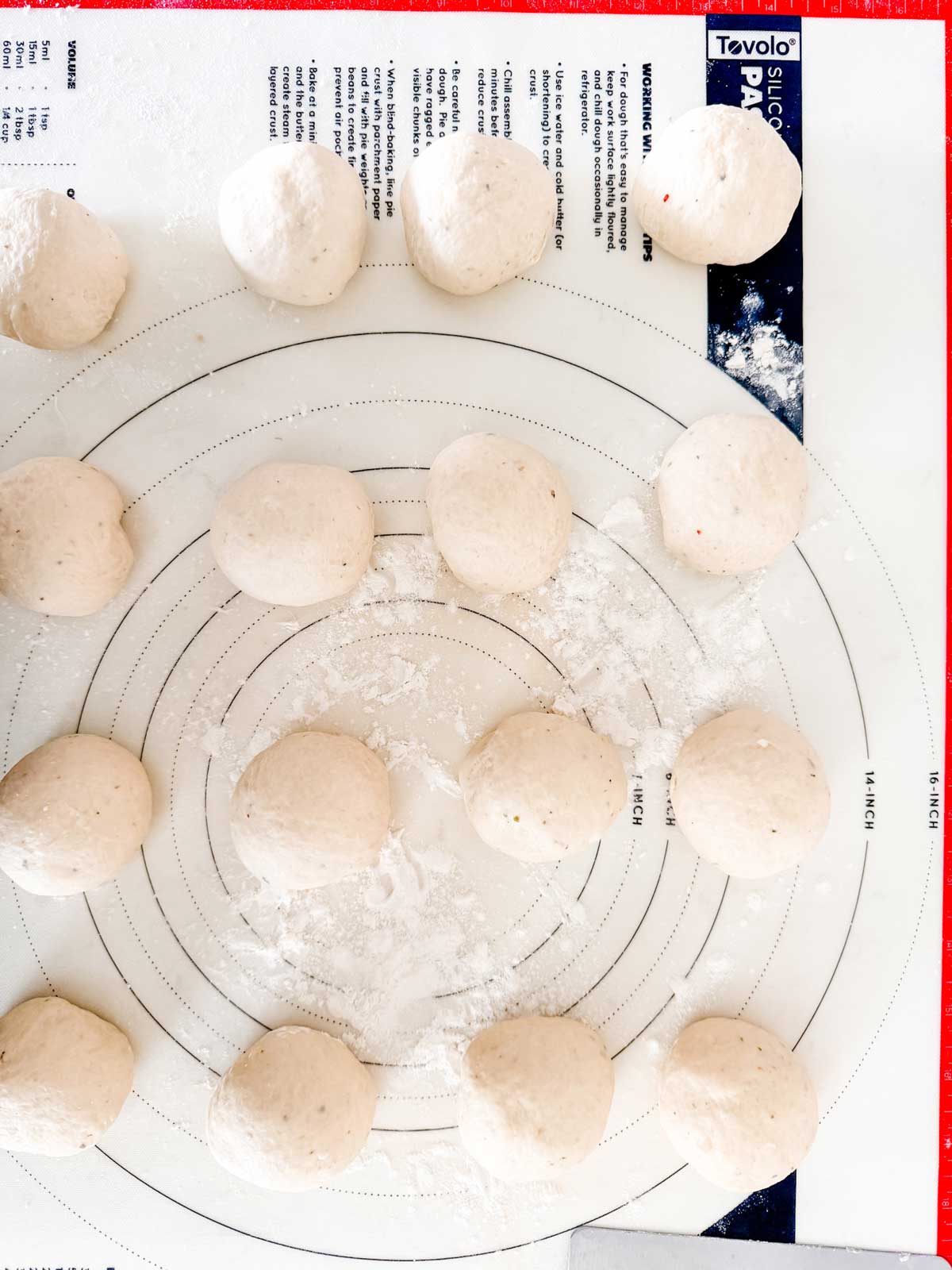 Several round dough balls are arranged on a floured silicone baking mat with circular measurement guides, ready to be shaped or baked.