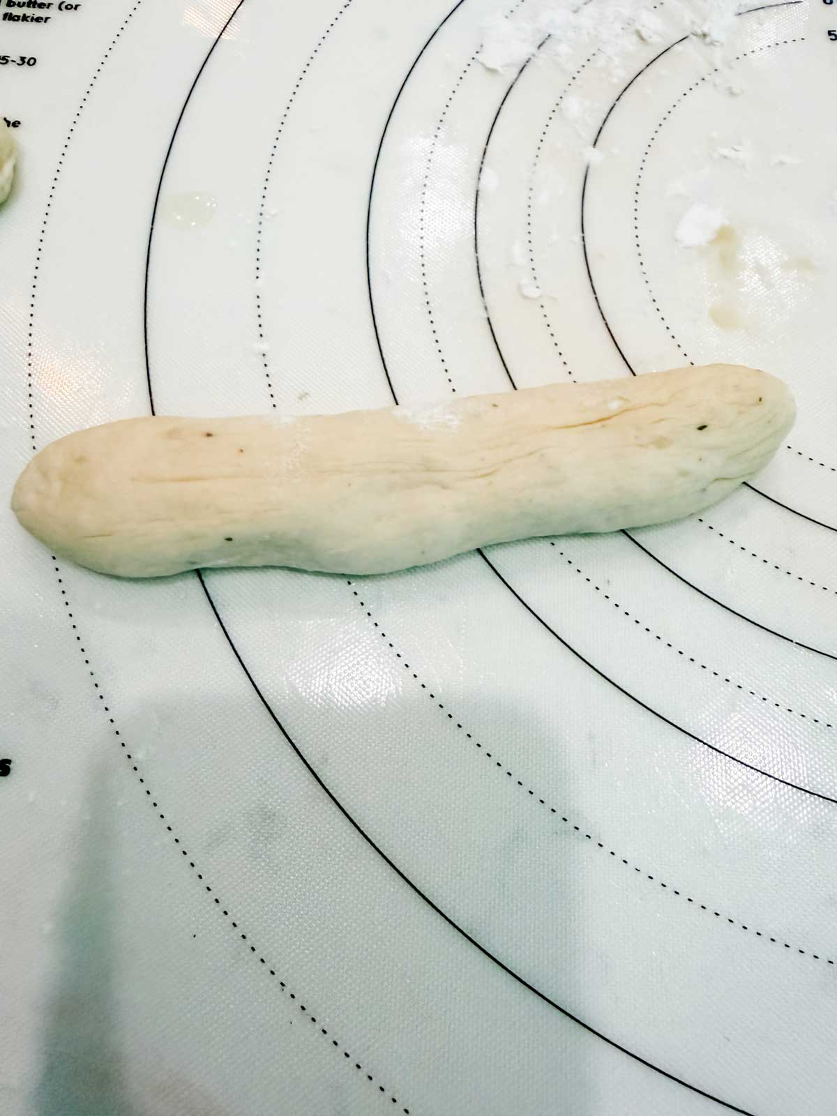 A piece of dough shaped into a short log rests on a white, circular measurement mat dusted lightly with flour.