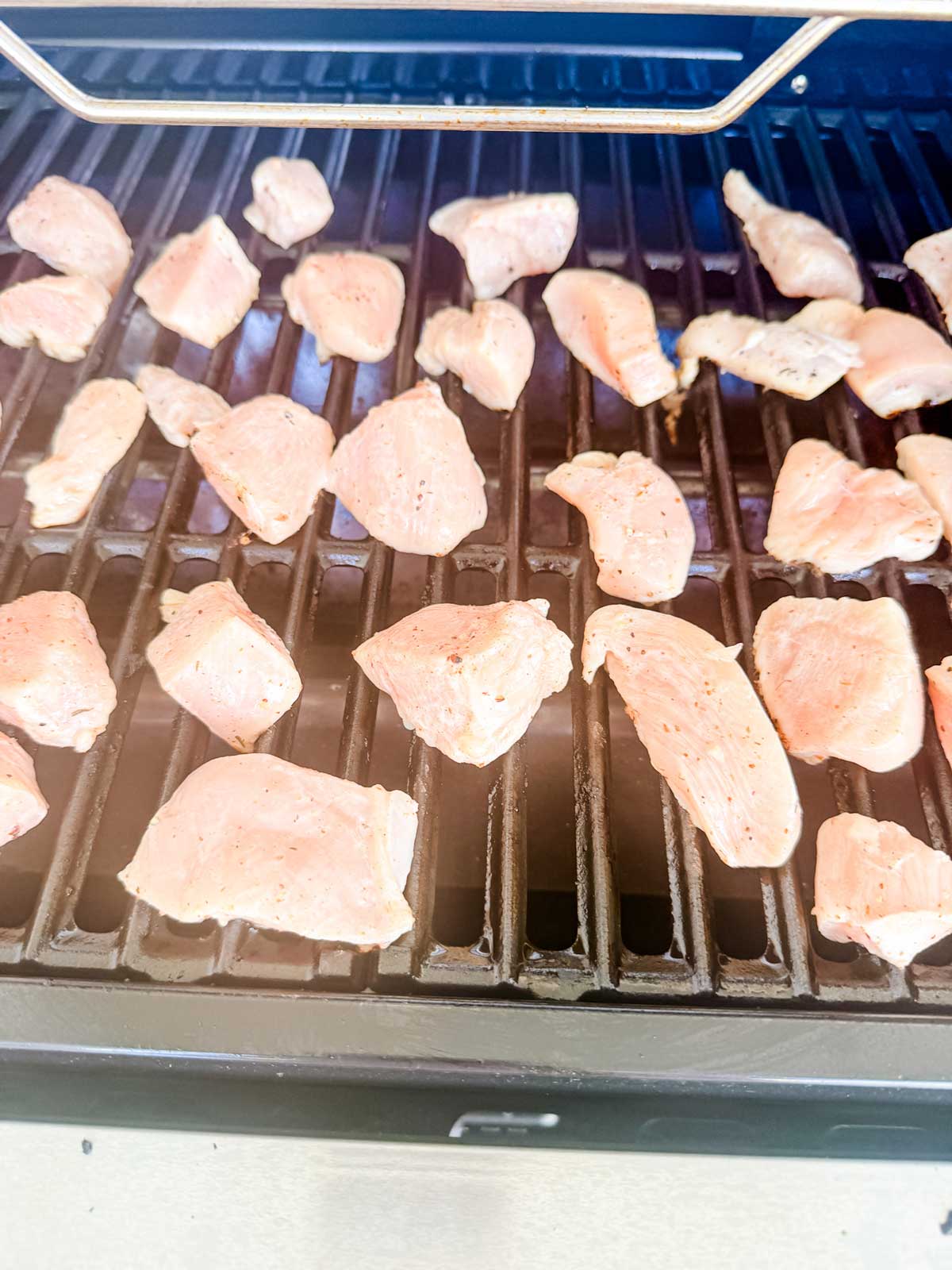 Raw, seasoned chicken pieces are spread out on the grates of an open outdoor grill, ready to be cooked.