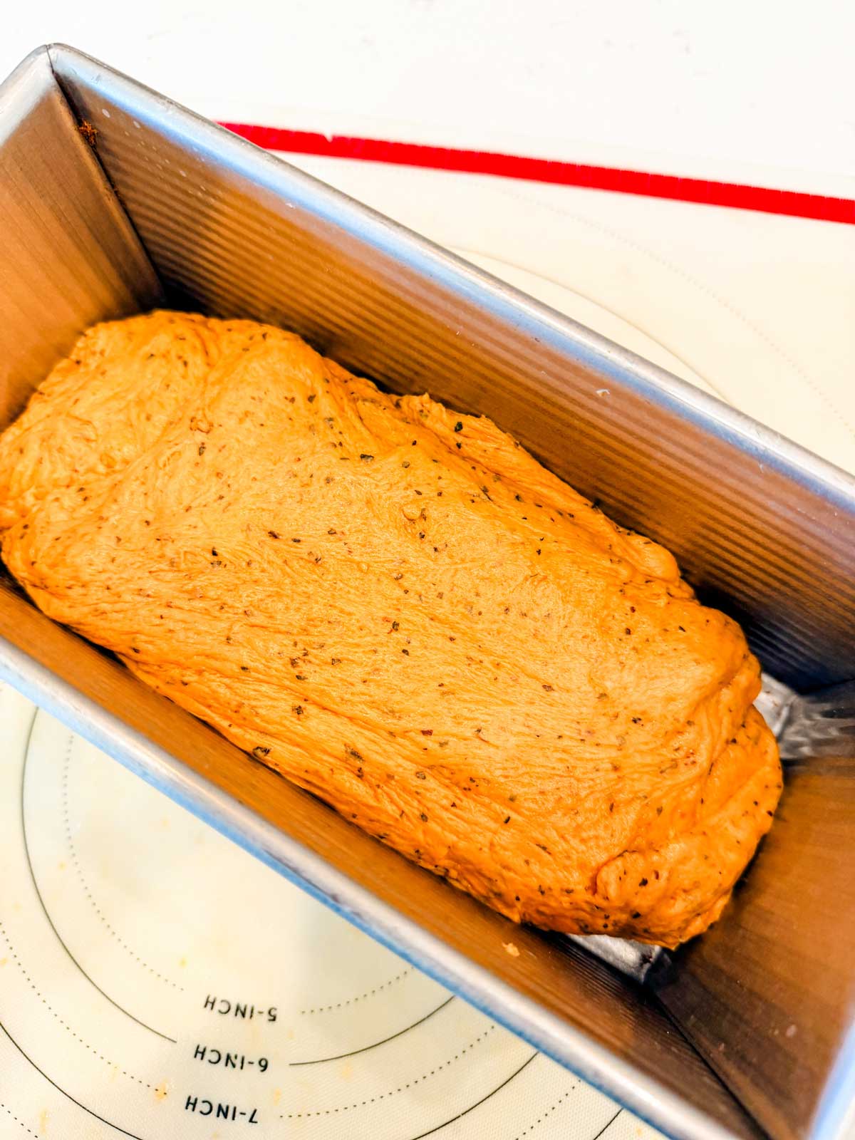 Unbaked bread dough with visible seasonings in a bread pan.